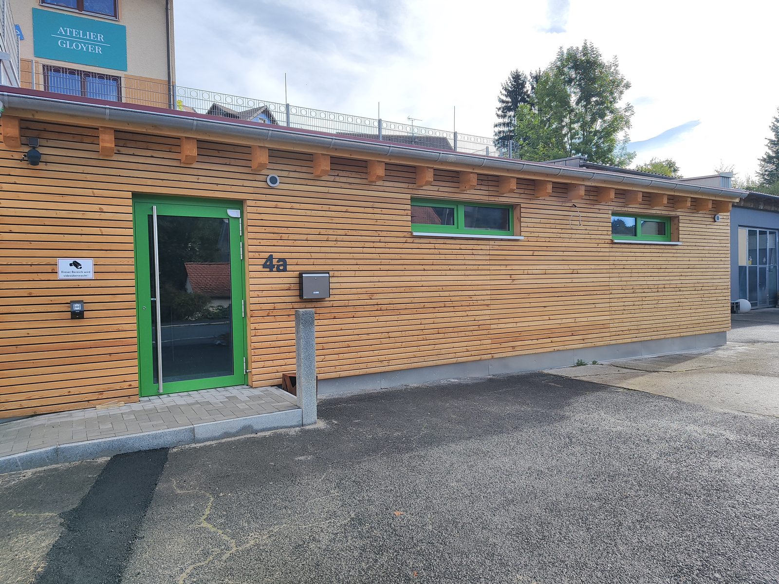 Der Kisi Shop von außen: Holzfassade aus Lärche mit grüner Eingangstür